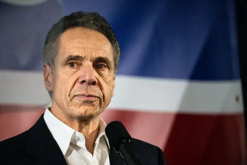 أندرو كومو يتحدث في مؤتمر صحفي، مع خلفية تحمل ألوان العلم الأمريكي، في إطار التحقيقات المتعلقة باستجابته لجائحة كوفيد-19.