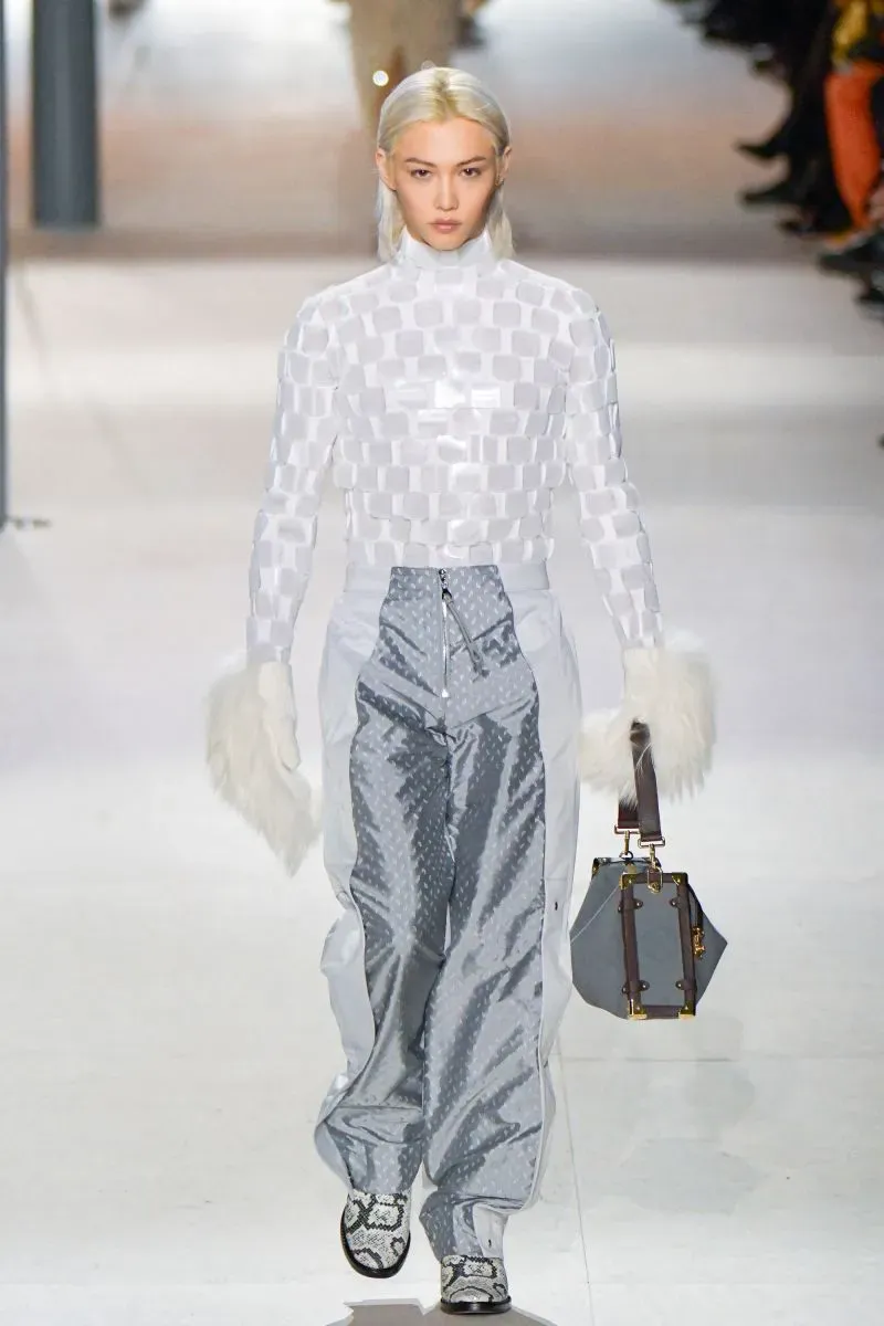 عارضة أزياء ترتدي ملابس عصرية باللونين الأبيض والرمادي، تسير على منصة عرض أزياء فاخرة خلال أسبوع الموضة في باريس.