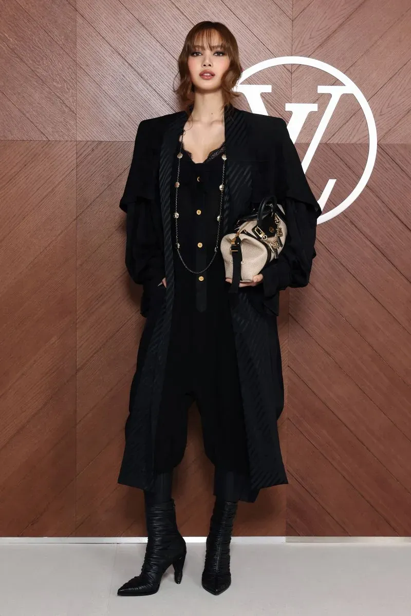 عارضة أزياء ترتدي ملابس سوداء أنيقة وتحمل حقيبة صغيرة، تقف أمام خلفية تحمل شعار لويس فويتون خلال أسبوع الموضة في باريس.