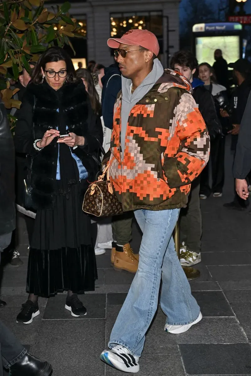 فنان مشهور يرتدي سترة ملونة وحقيبة لويس فويتون، يتجول في حشود أسبوع الموضة في باريس، مع امرأة ترتدي ملابس سوداء بجواره.