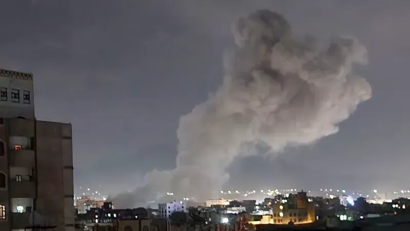 دخان كثيف يتصاعد من منطقة حضرية في اليمن ليلاً، مما يعكس تأثير الضربات العسكرية الأمريكية على الوضع الأمني في البلاد.