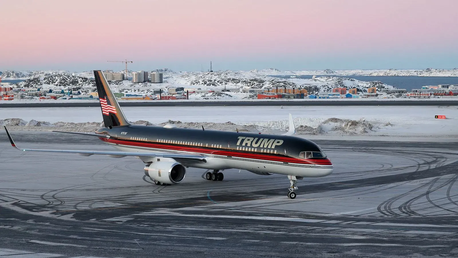 طائرة ترامب الخاصة على مدرج مطار في غرينلاند، مع خلفية ثلجية ومبانٍ ملونة، تعكس التوترات السياسية حول الاستحواذ على الجزيرة.