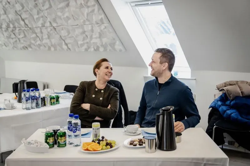 رئيسة الوزراء الدنماركية ميتي فريدريكسن تتحدث مع ينس فريدريك نيلسن في اجتماع في غرينلاند، مع تقديم مشروبات ووجبات خفيفة تعكس التعاون بين الجانبين.