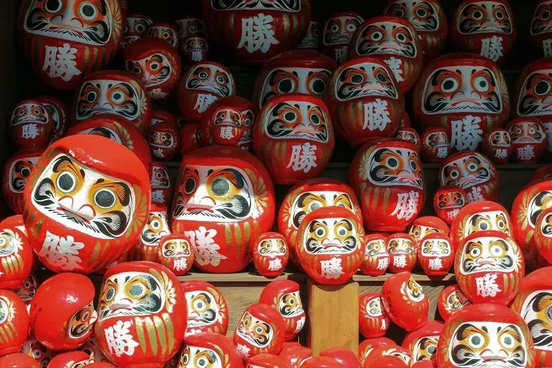 دمى داروما الحمراء مستديرة الشكل، تتجمع في مجموعة، تمثل رمز المثابرة والنجاح في الثقافة اليابانية.