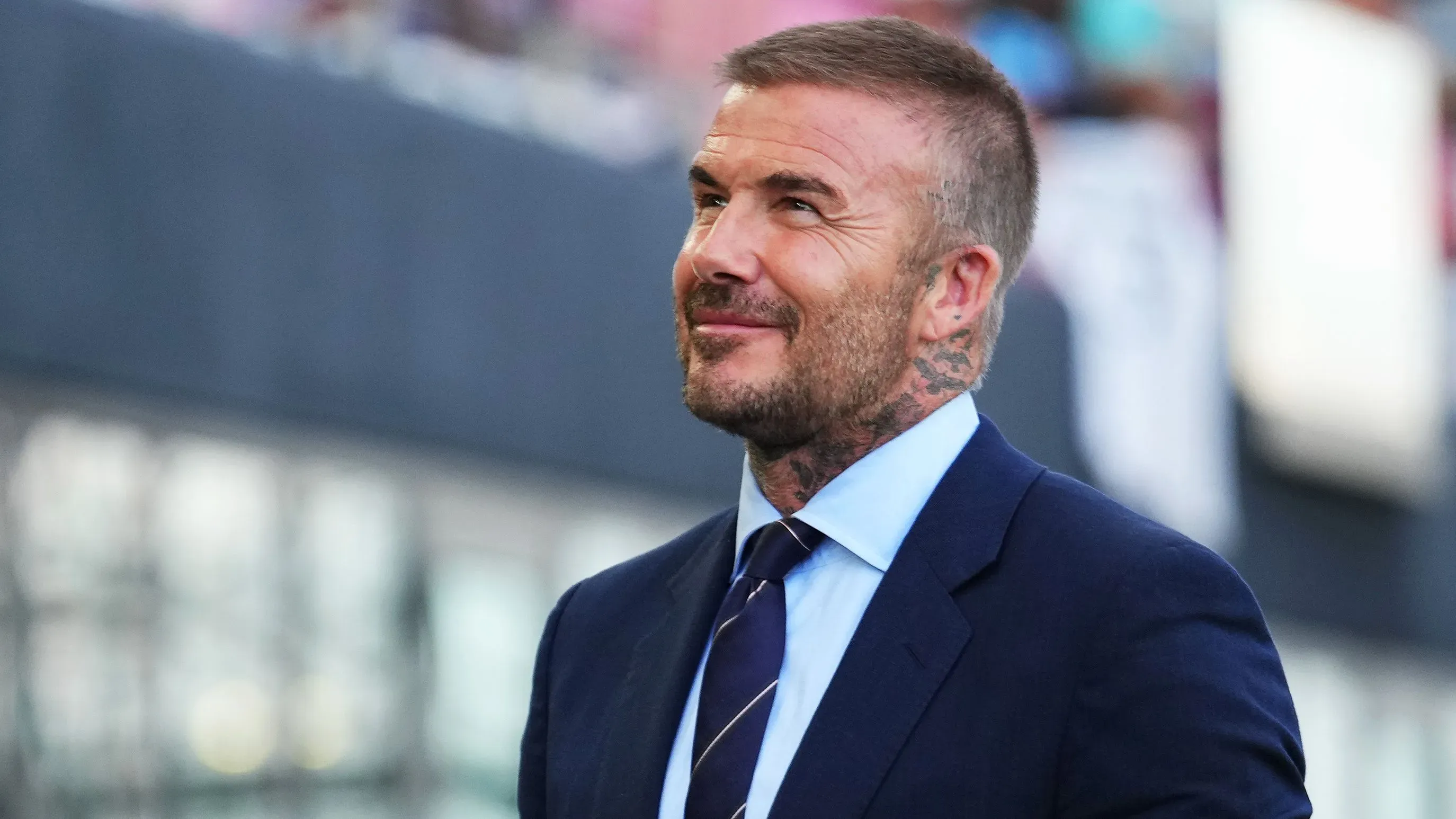 ديفيد بيكهام مبتسم في بدلة رسمية، يعكس لحظة طريفة بعد قص شعره الذي أدى إلى ظهور بقعة صلعاء، مما أثار تعليقات زوجته فيكتوريا.