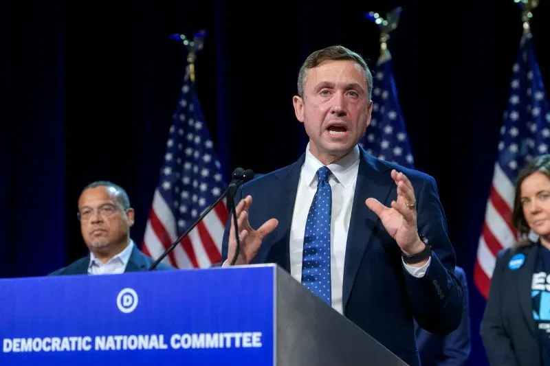 كين مارتن، رئيس اللجنة الوطنية الديمقراطية، يتحدث خلال مؤتمر صحفي، مع أعضاء آخرين في الخلفية، أمام لافتة الحزب.