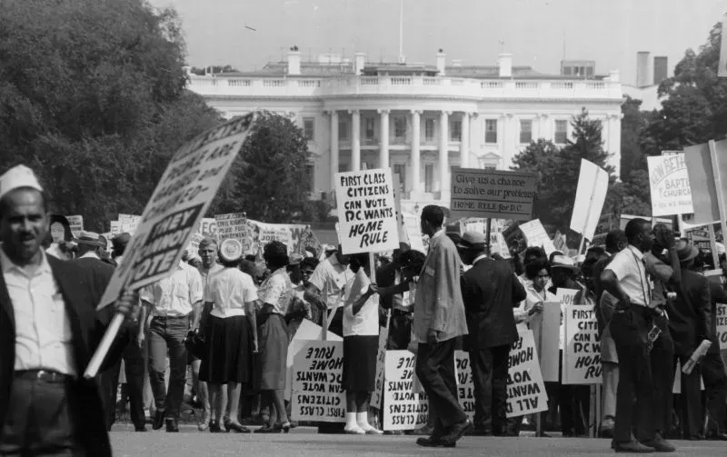 مظاهرة تاريخية أمام البيت الأبيض تطالب بحقوق المواطنين في العاصمة واشنطن، مع لافتات تدعو إلى الحكم الذاتي والتصويت.
