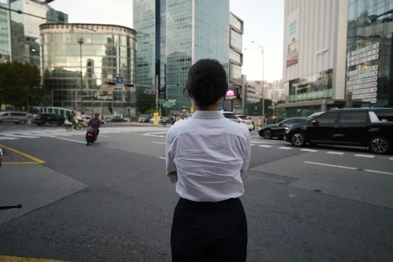 امرأة ترتدي قميصًا أبيض وسروالًا أسود، تقف في الشارع أمام ناطحات سحاب في مدينة حديثة، تعكس التحديات التي تواجهها ضحايا الجرائم الجنسية الرقمية.