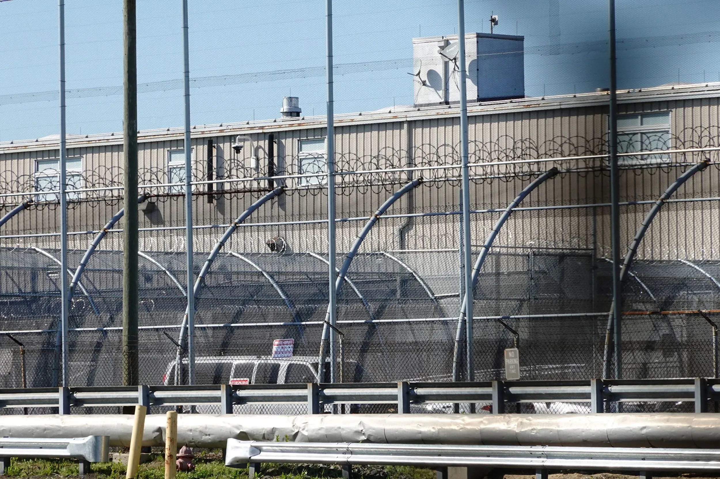 مركز احتجاز مهاجرين محاط بأسلاك شائكة، يظهر فيه المبنى الفيدرالي مع علامات تحذيرية، يرمز إلى قضايا الرقابة والممارسات القانونية.