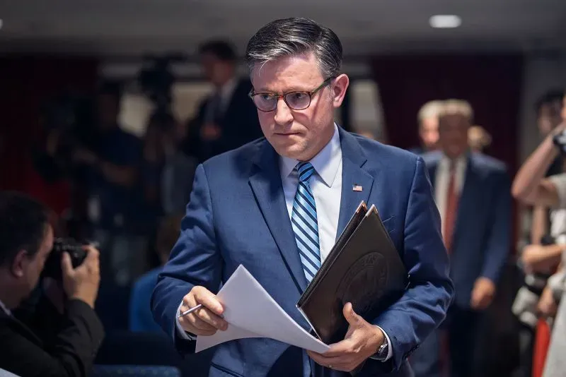 رجل يرتدي بدلة رسمية يحمل أوراقًا، يبدو جادًا أثناء مغادرته قاعة مؤتمرات، مما يعكس أجواء السياسة الأمريكية الحالية.