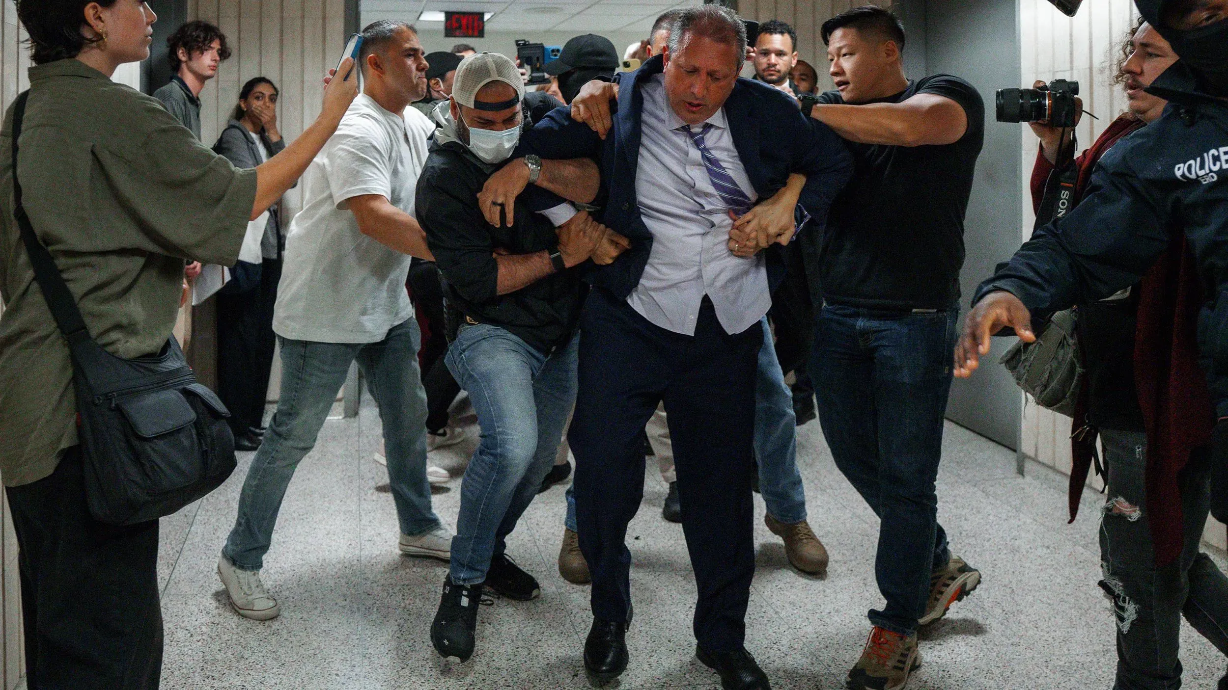 اعتقال مسؤول حكومي وسط احتجاجات على سياسات الهجرة، مع تواجد حشد من المتظاهرين والمصورين في الخلفية.