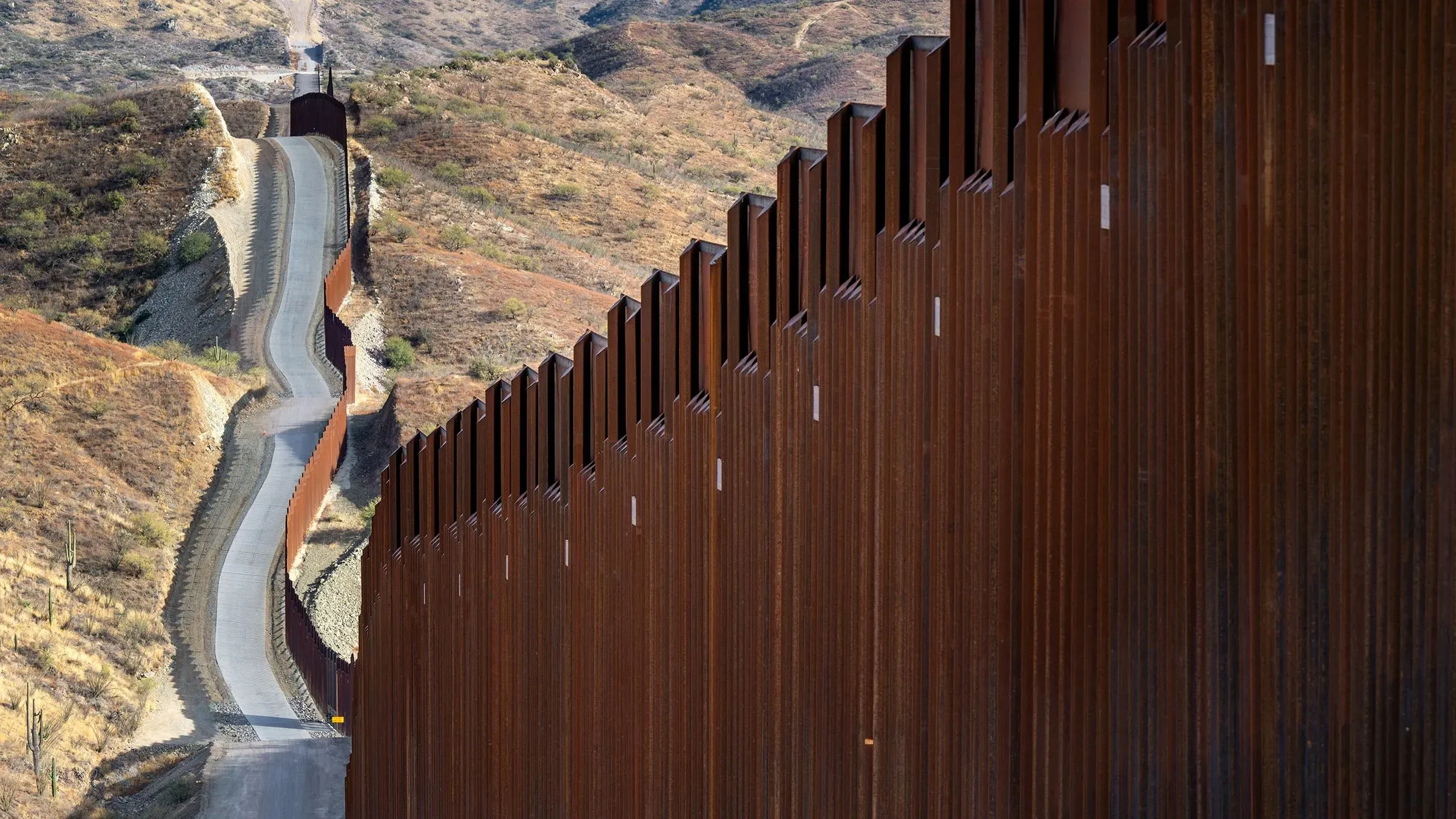 جدار حدودي يمتد عبر تلال جافة، يمثل جزءًا من النقاش حول قوانين الهجرة الجديدة في الولايات المتحدة.