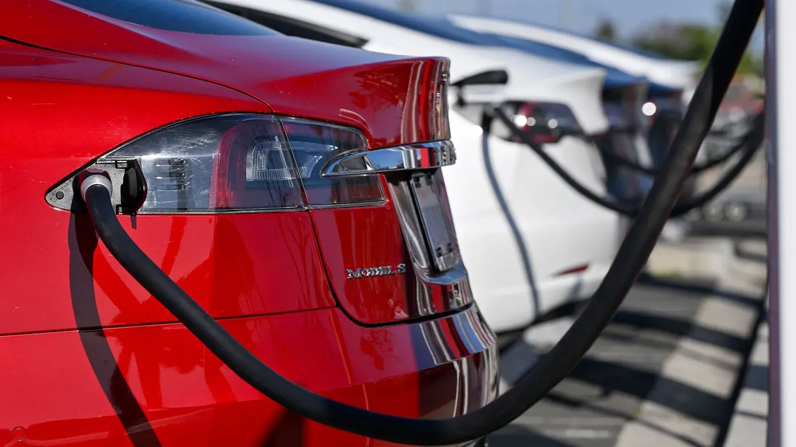 سيارة كهربائية حمراء متصلة بشاحن، مع سيارات أخرى في الخلفية، تعكس جهود كاليفورنيا للحد من انبعاثات السيارات.