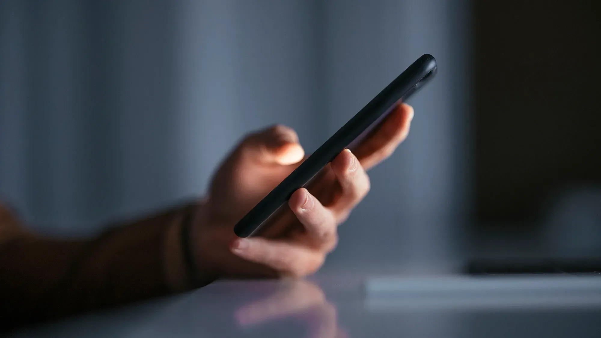 يد تحمل هاتفا ذكيا مضاء في بيئة مظلمة، مما يعكس القلق حول استخدام الذكاء الاصطناعي في إنشاء محتوى مزيف.