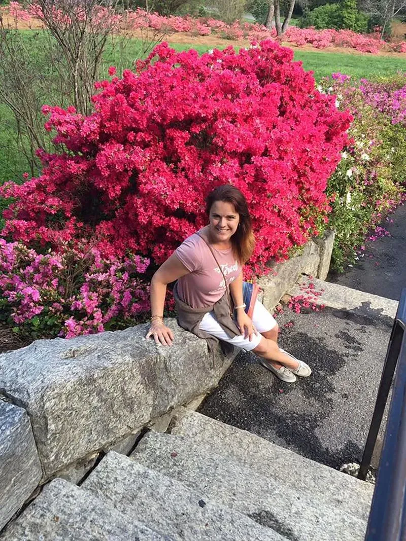 امرأة تجلس على درج حجري أمام أزهار زاهية، مما يضفي جوًا من الجمال الطبيعي في سياق قضية جريمة قتل في كولورادو.