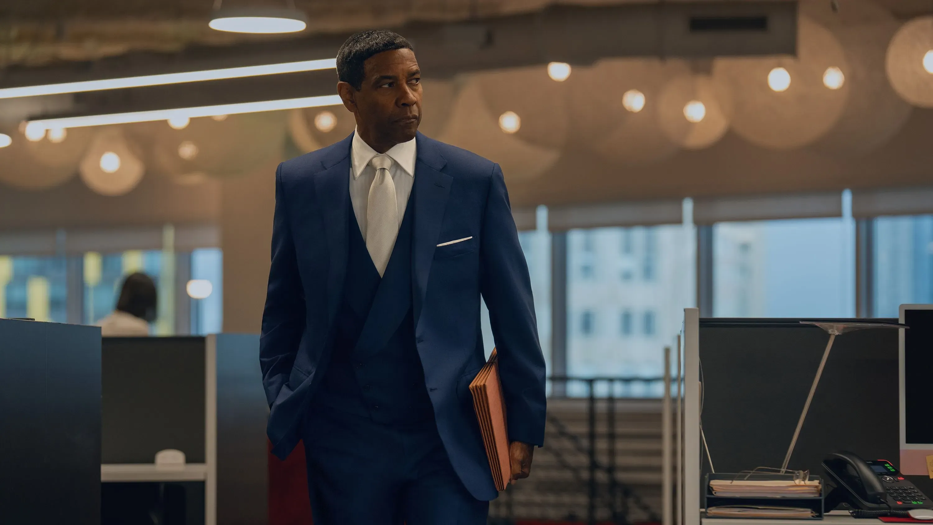 دينزل واشنطن يرتدي بدلة أنيقة أثناء تجوله في مكتب حديث، مع إضاءة دافئة وخلفية تعكس أجواء العمل في صناعة الموسيقى.