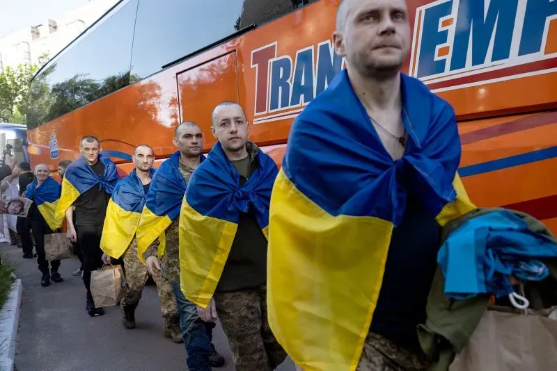 رجال أوكرانيون يرتدون علم بلادهم، يسيرون نحو حافلة بعد إطلاق سراحهم في إطار تبادل سجناء، وسط أجواء من الأمل والتوتر.