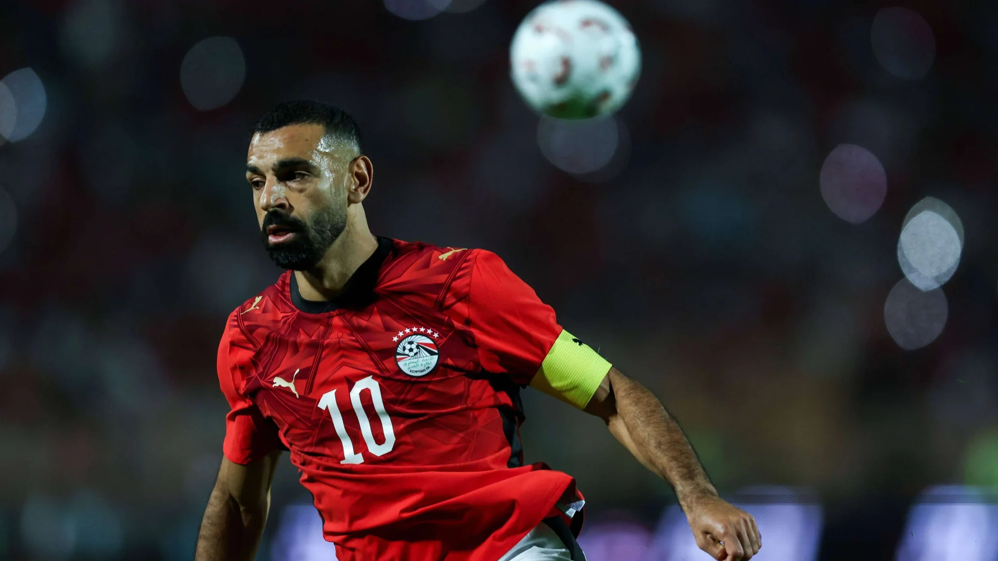 محمد صلاح قائد منتخب مصر يرتدي شارة القيادة ويركز على الكرة خلال مباراة رسمية، في ظل أزمة غيابه عن مباريات المنتخب الأخيرة.