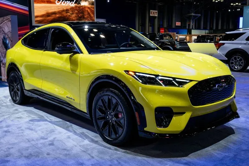 سيارة فورد كهربائية صفراء حديثة مع تصميم رياضي، معروضة في معرض للسيارات، تعكس التوجه نحو الابتكار في صناعة السيارات.