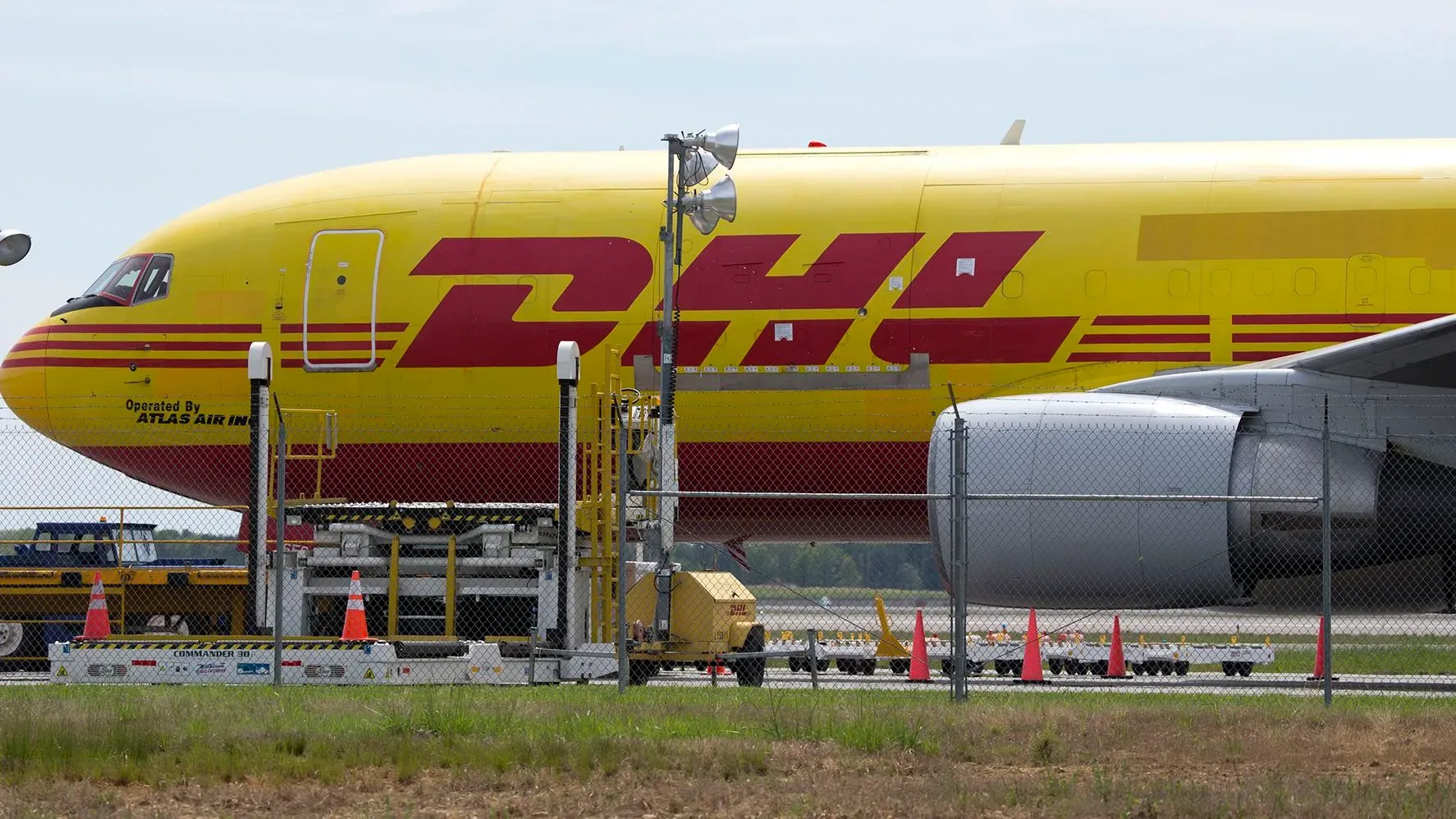 طائرة شحن تابعة لشركة DHL، تحمل اللونين الأصفر والأحمر، متوقفة على مدرج المطار، مع معدات الشحن حولها.