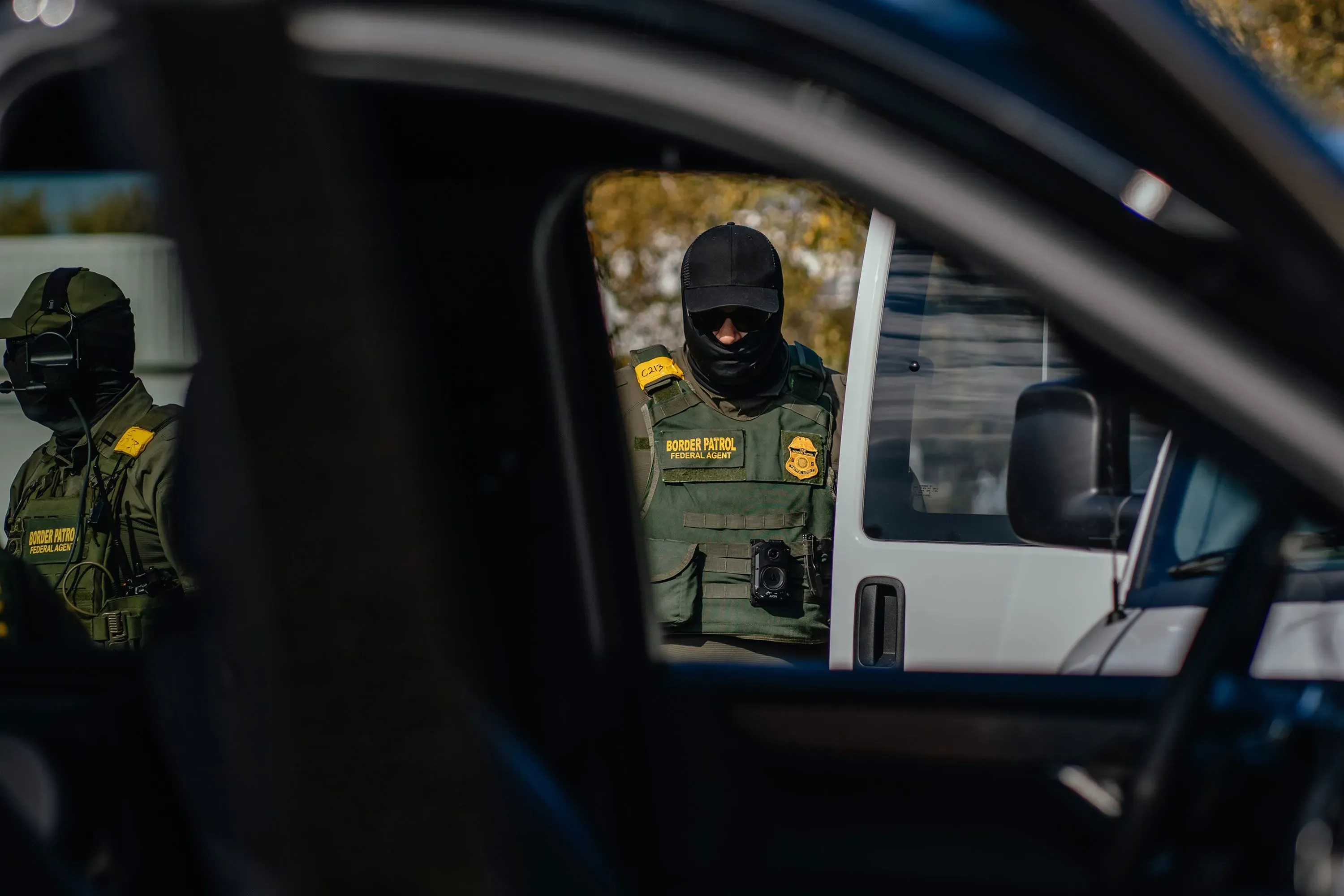 عناصر من إدارة الهجرة يقفون بالقرب من سيارة أثناء مداهمة، مما يعكس التوترات المحيطة بقضايا الهجرة في الولايات المتحدة.