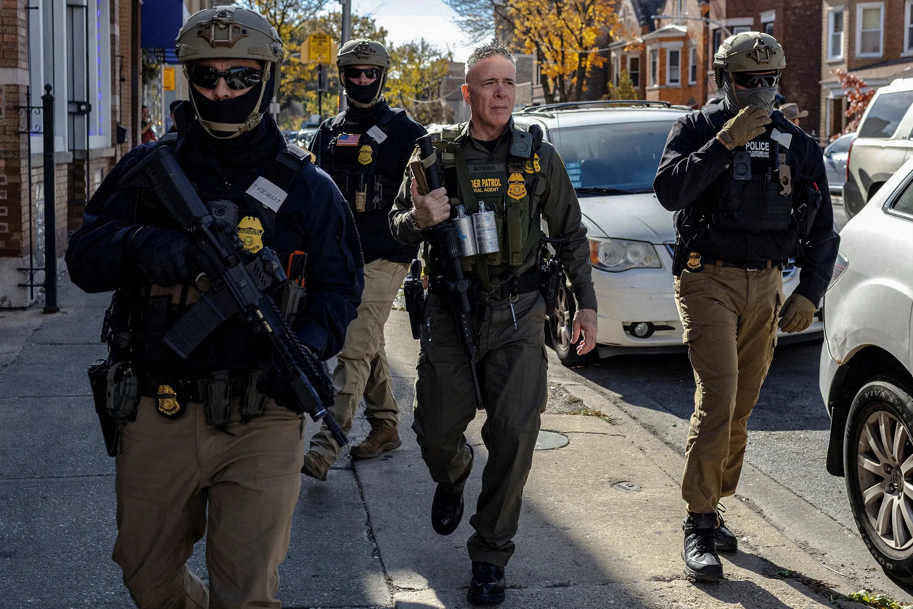 رجال مسلحون من إدارة الهجرة والجمارك يسيرون في شارع، مما يعكس أجواء التوتر المرتبطة بعمليات الاعتقال في شيكاغو.