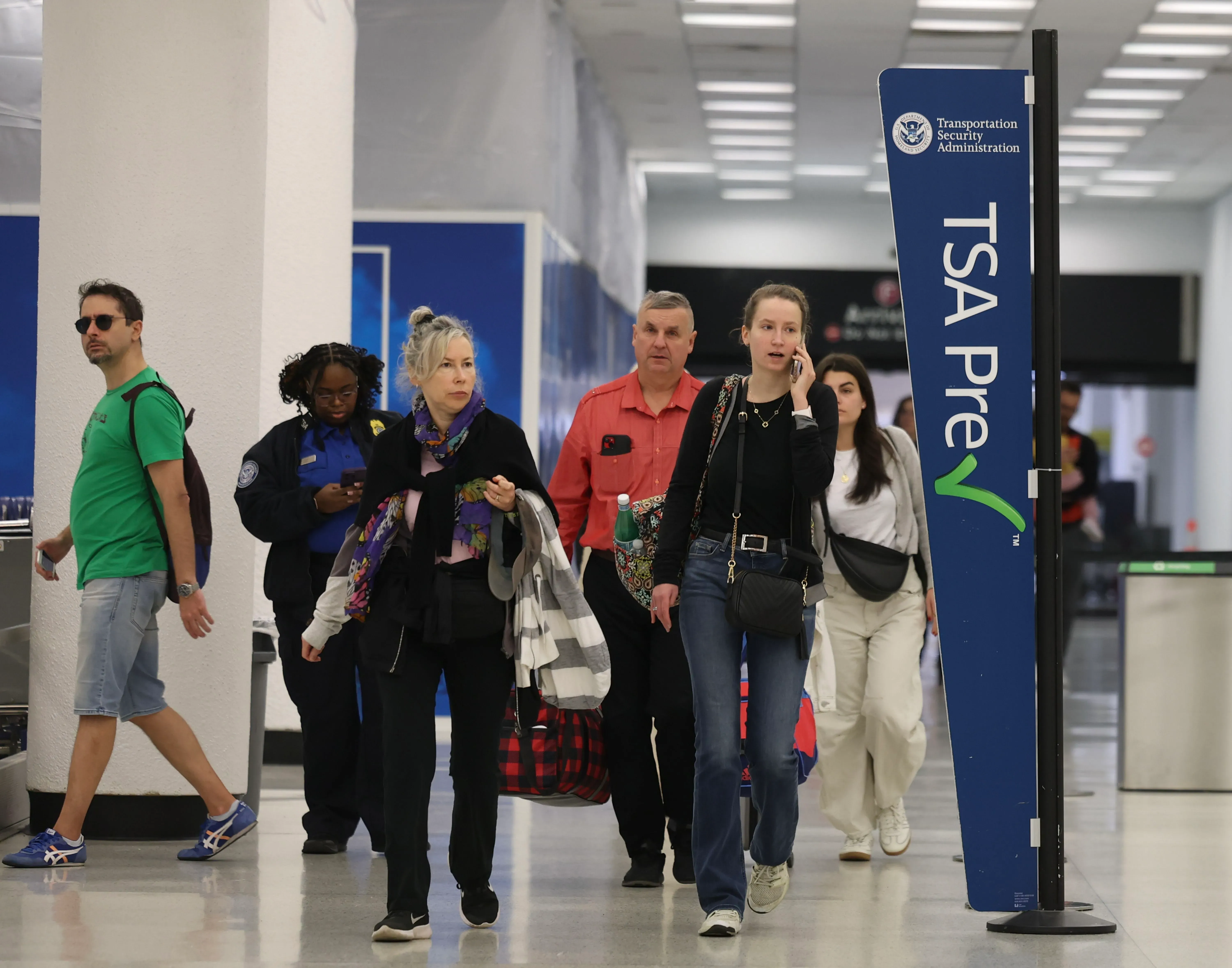تظهر الصورة مسافرين في مطار يتجهون نحو ممر TSA PreCheck، مع وجود علامة واضحة تشير إلى البرنامج. يعكس هذا السياق تأثير الإغلاق الحكومي على إجراءات السفر.