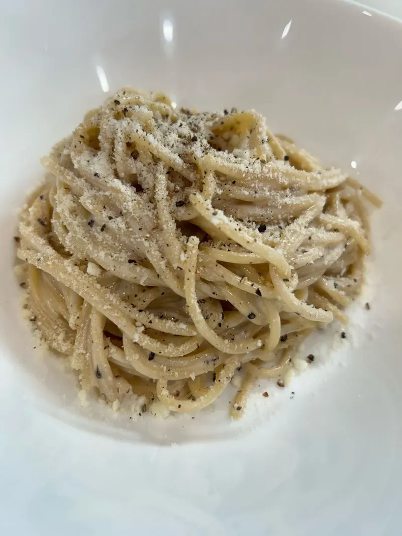 طبق المعكرونة كاسيو إي بيبي، مزين بالجبن والفلفل الأسود، يُظهر توازنًا دقيقًا بين المكونات في وعاء أبيض.