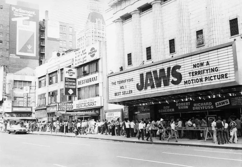 طابور طويل من الناس أمام دار عرض فيلم "الفك المفترس"، مع لافتة كبيرة تعلن عن الفيلم كـ"فيلم رعب مرعب".