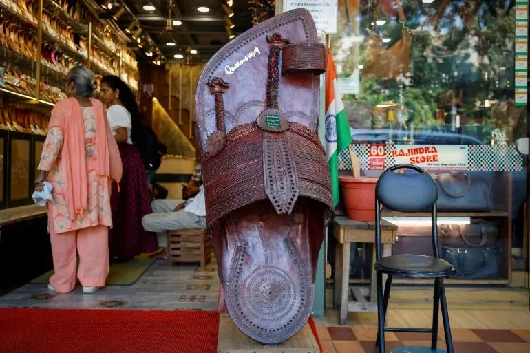 صندل كولهابوري تقليدي كبير مع تفاصيل دقيقة، مع وجود زبائن في متجر للأحذية في الخلفية، يعكس التراث الثقافي لصناعة الصنادل في الهند.