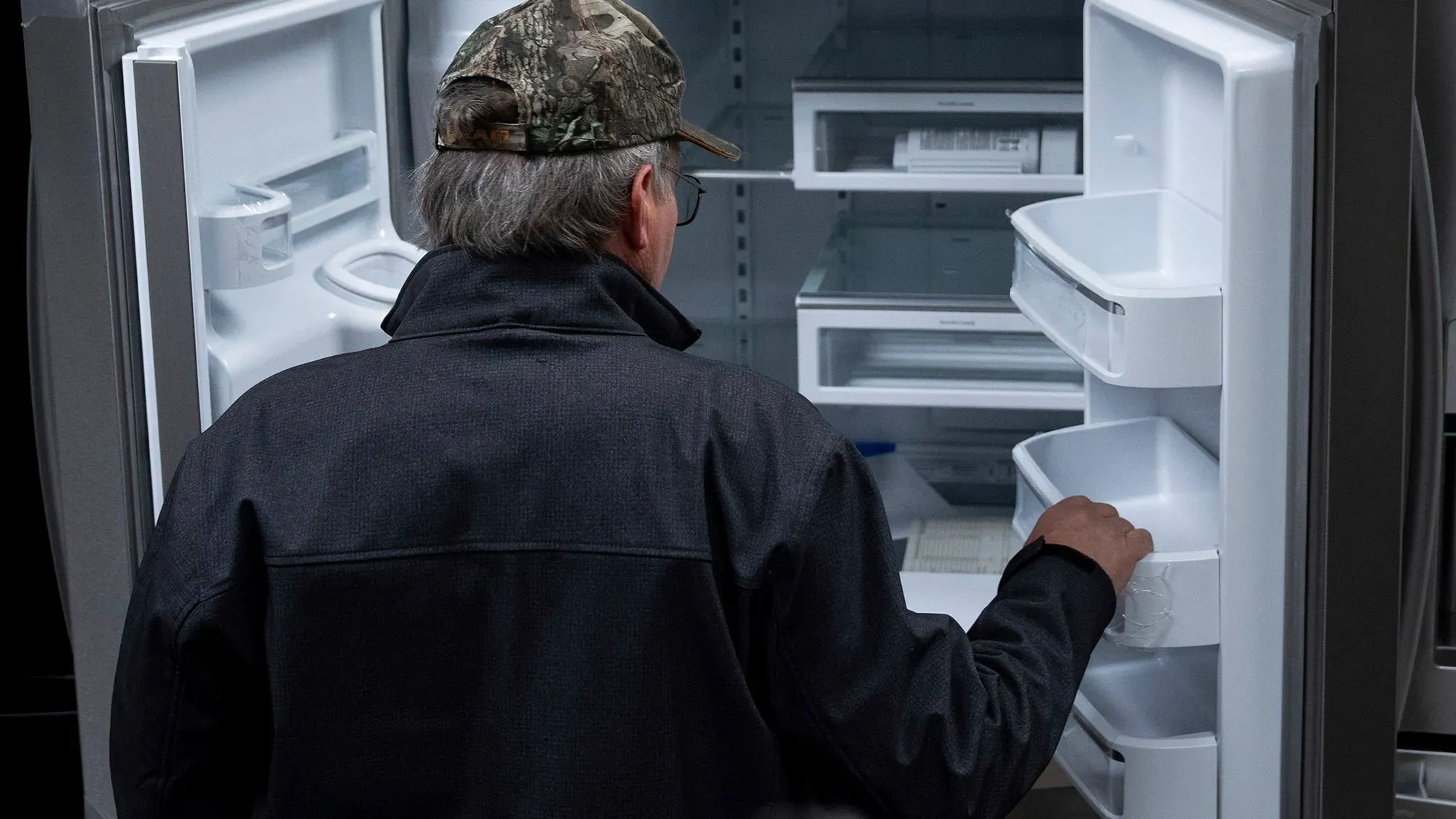 رجل يرتدي قبعة يتفقد ثلاجة فارغة، مما يعكس تزايد إنفاق الأمريكيين على السلع باهظة الثمن وسط مخاوف من التعريفات الجمركية.