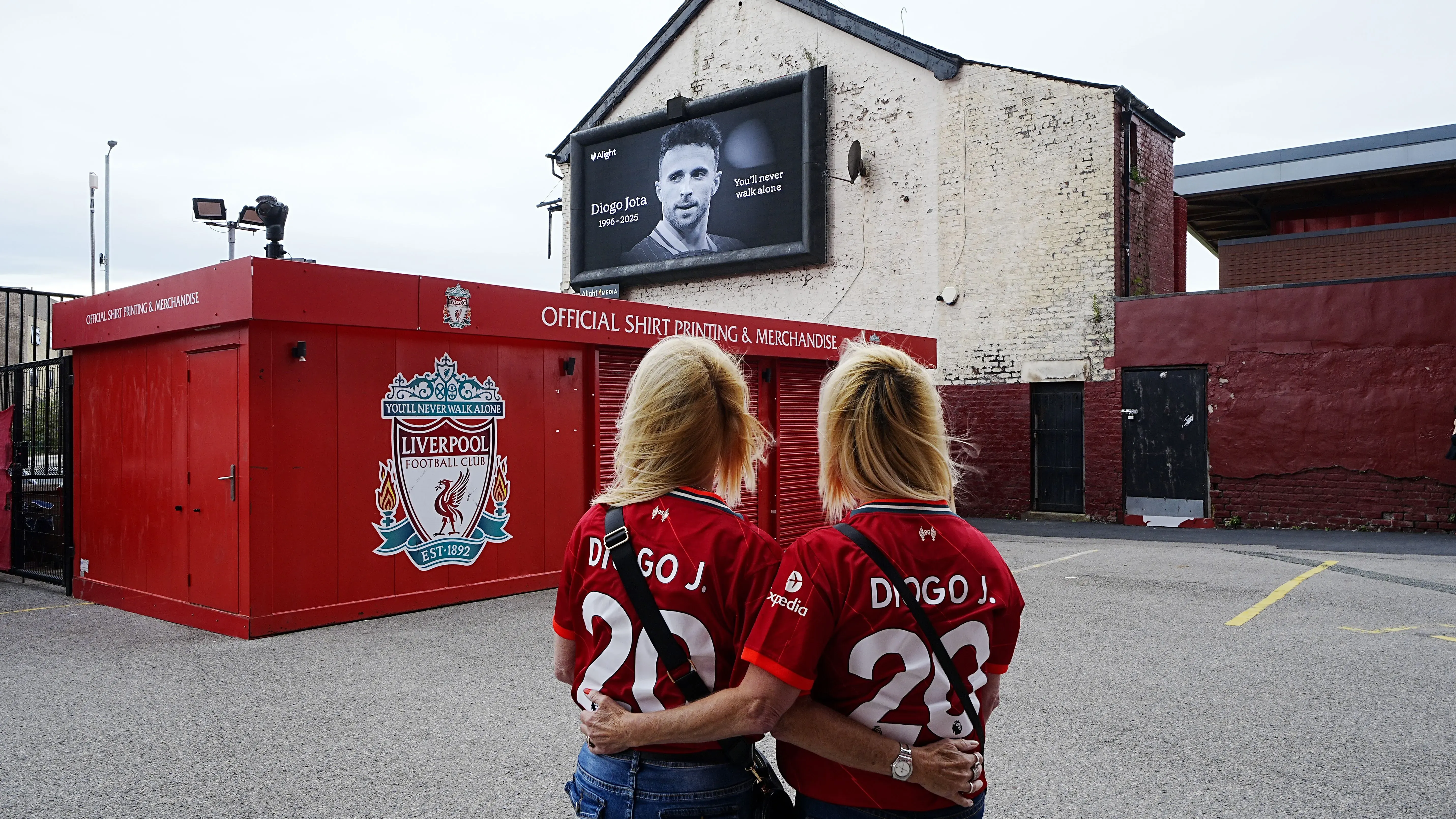 امرأتان ترتديان قمصان ليفربول الحمراء، تحملان اسم "دييغو جوتا"، يقفان أمام متجر النادي، مع صورة لجوتا على الشاشة خلفهما.