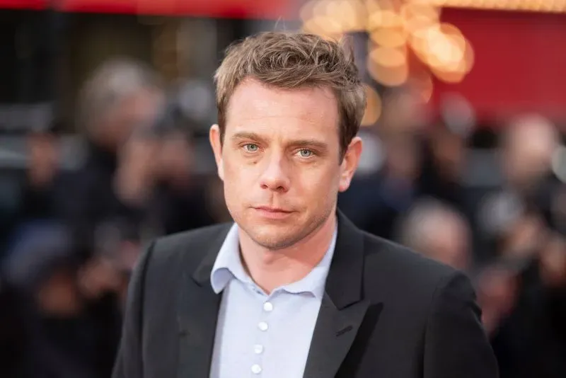 جوناثان أندرسون، المصمم الجديد لدار ديور للأزياء الرجالية، يظهر في حدث عام، مع خلفية ضبابية لمصورين ومشاهدين.