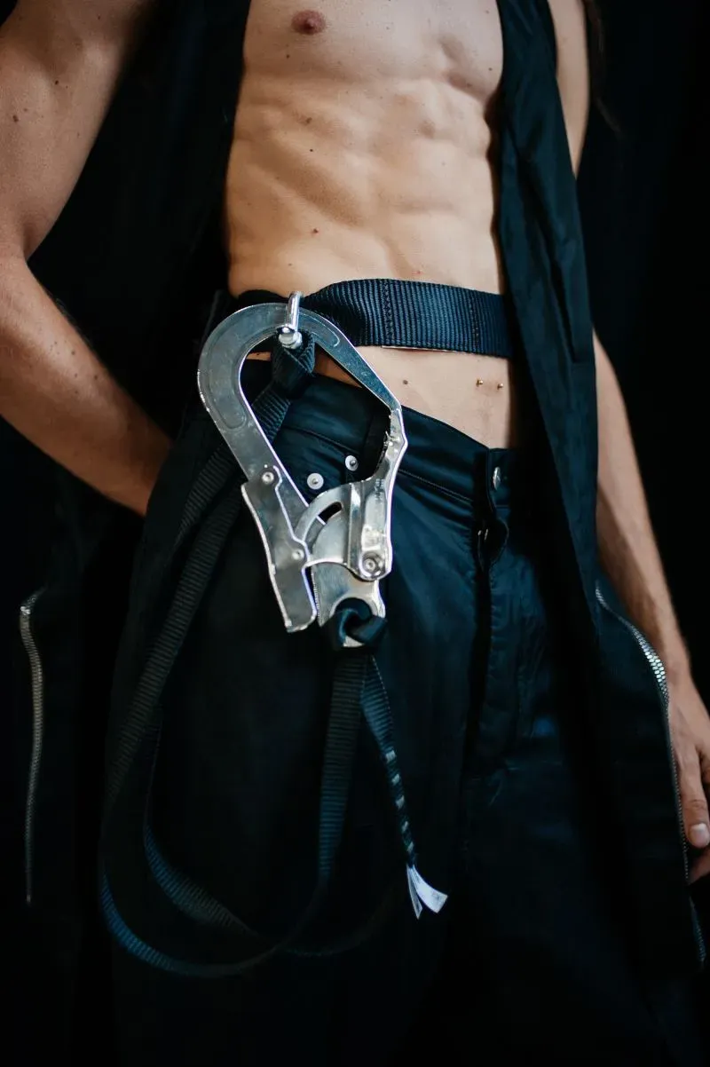 تصميم مبتكر لملابس رجالية، يظهر شخص يرتدي بنطالاً أسود مع حزام معدني، يعكس تأثير الأزياء المعاصرة والموضة القابلة للتكيف.