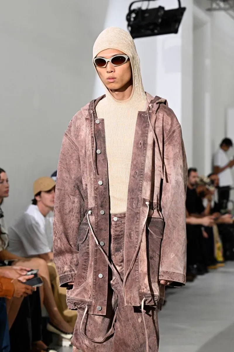 عارض شاب يرتدي ملابس عصرية بتدرجات اللون البني، مع نظارات شمسية، خلال عرض أزياء في أسبوع الموضة في باريس.