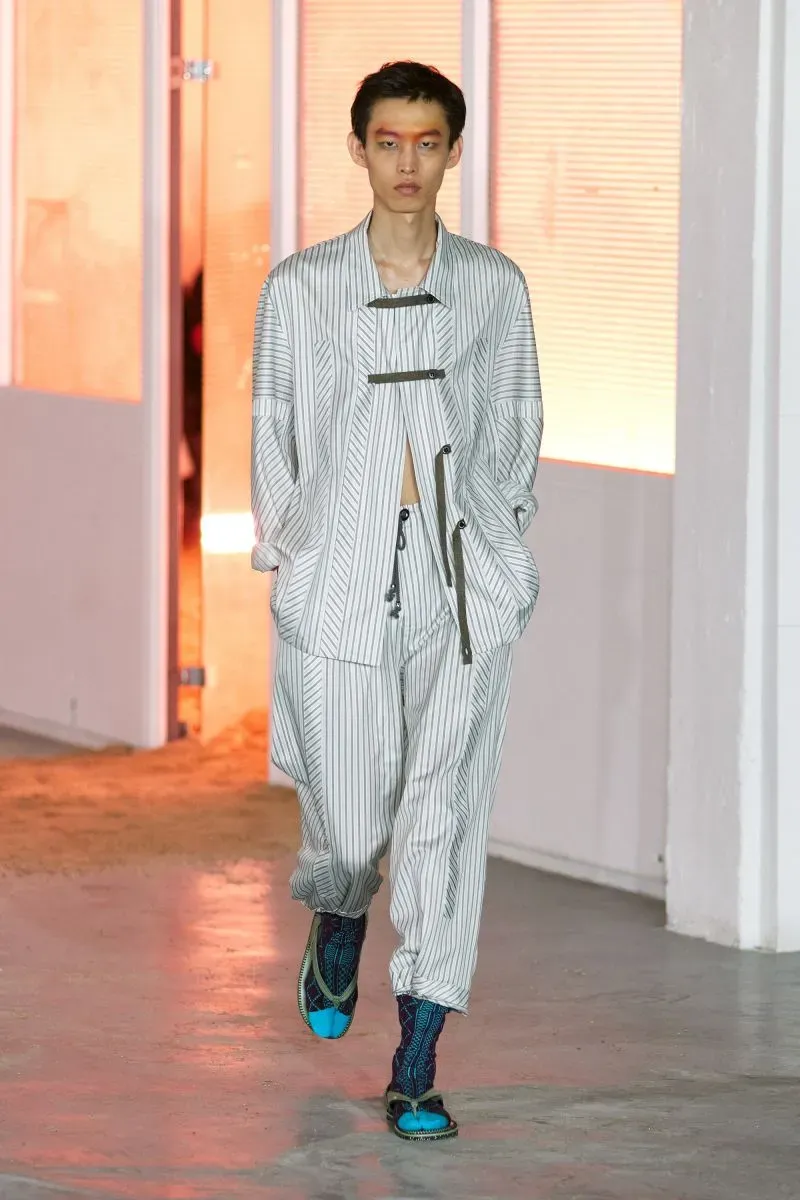 عارض شاب أزياءً عصرية ذات خطوط عمودية في عرض أزياء في باريس، مع لمسات جريئة في التصميم والألوان.