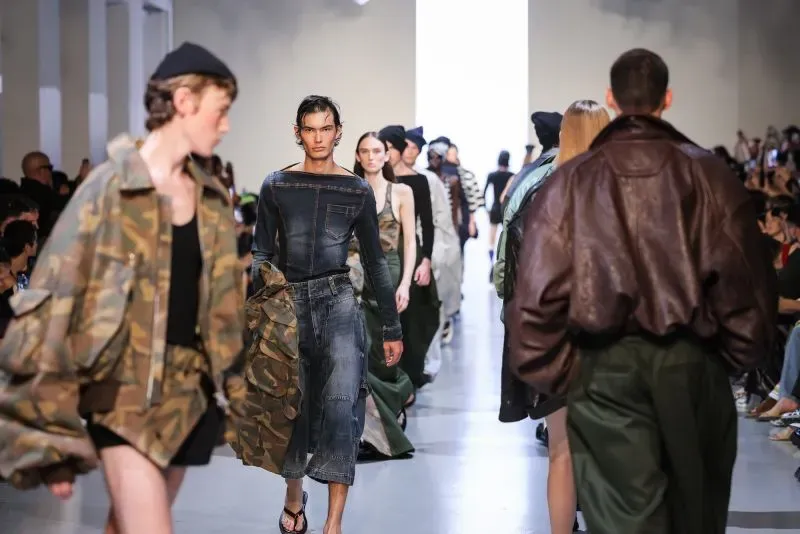 مجموعة من العارضين في عرض أزياء باريس، يرتدون ملابس عصرية تجمع بين الألوان الزاهية والتصاميم الفريدة، مع تركيز على الأناقة والراحة.