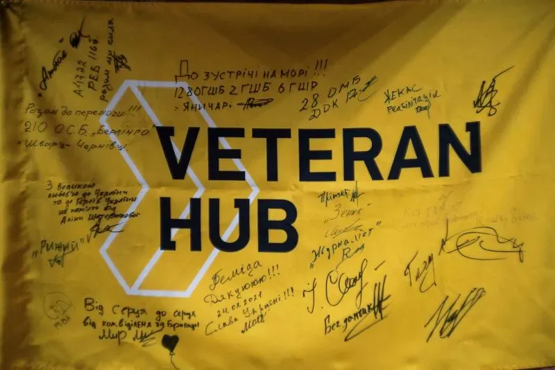 علم أصفر يحمل عبارة "VETERAN HUB" مع توقيعات ورسائل من أفراد، يعكس دعم المجتمع للمحاربين القدامى في أوكرانيا.