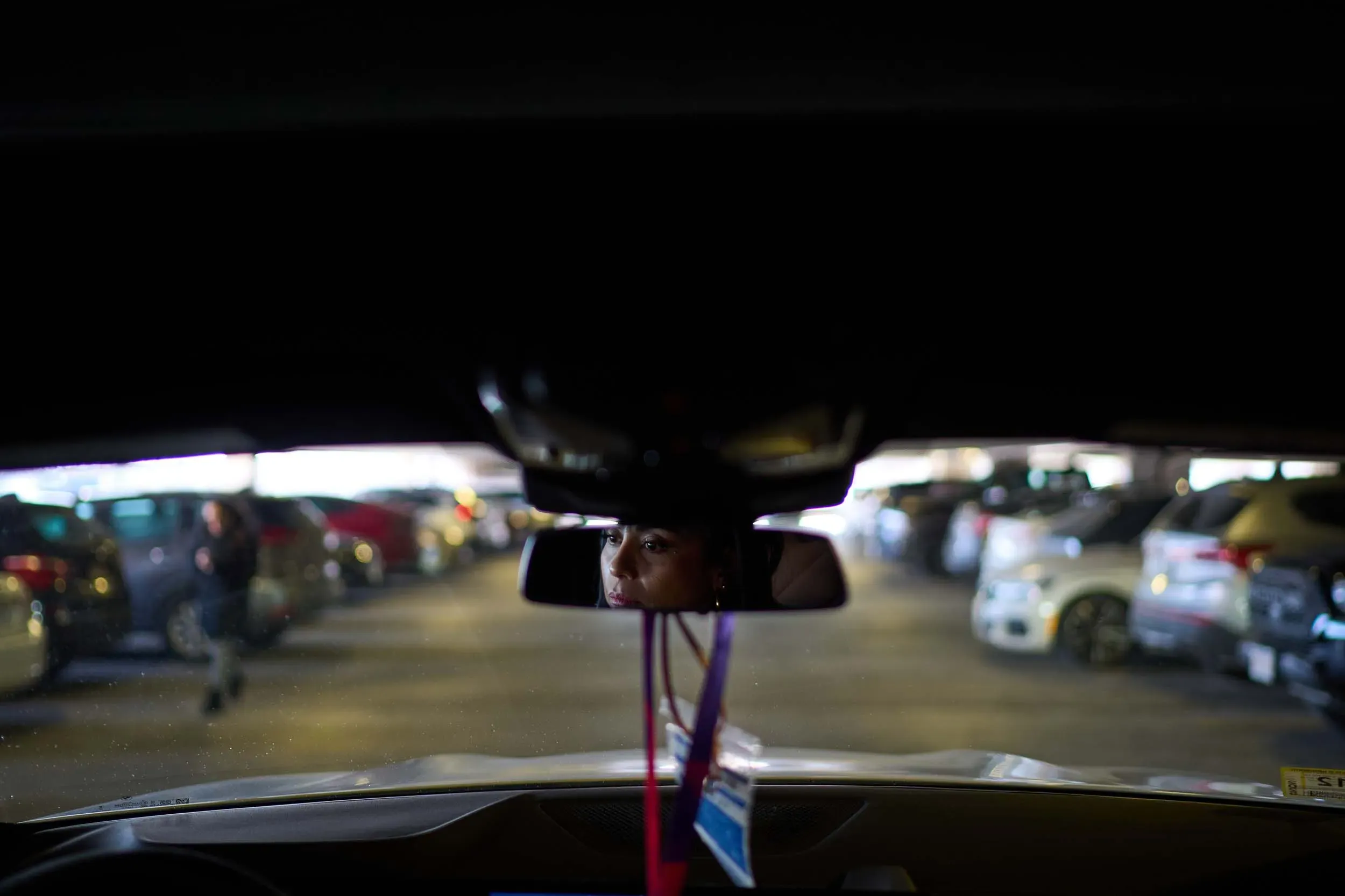 امرأة تنظر من داخل سيارتها في موقف سيارات مظلم، مع رؤية محدودة للسيارات المحيطة بها، تعكس تحديات الحياة مع مرض الذئبة.