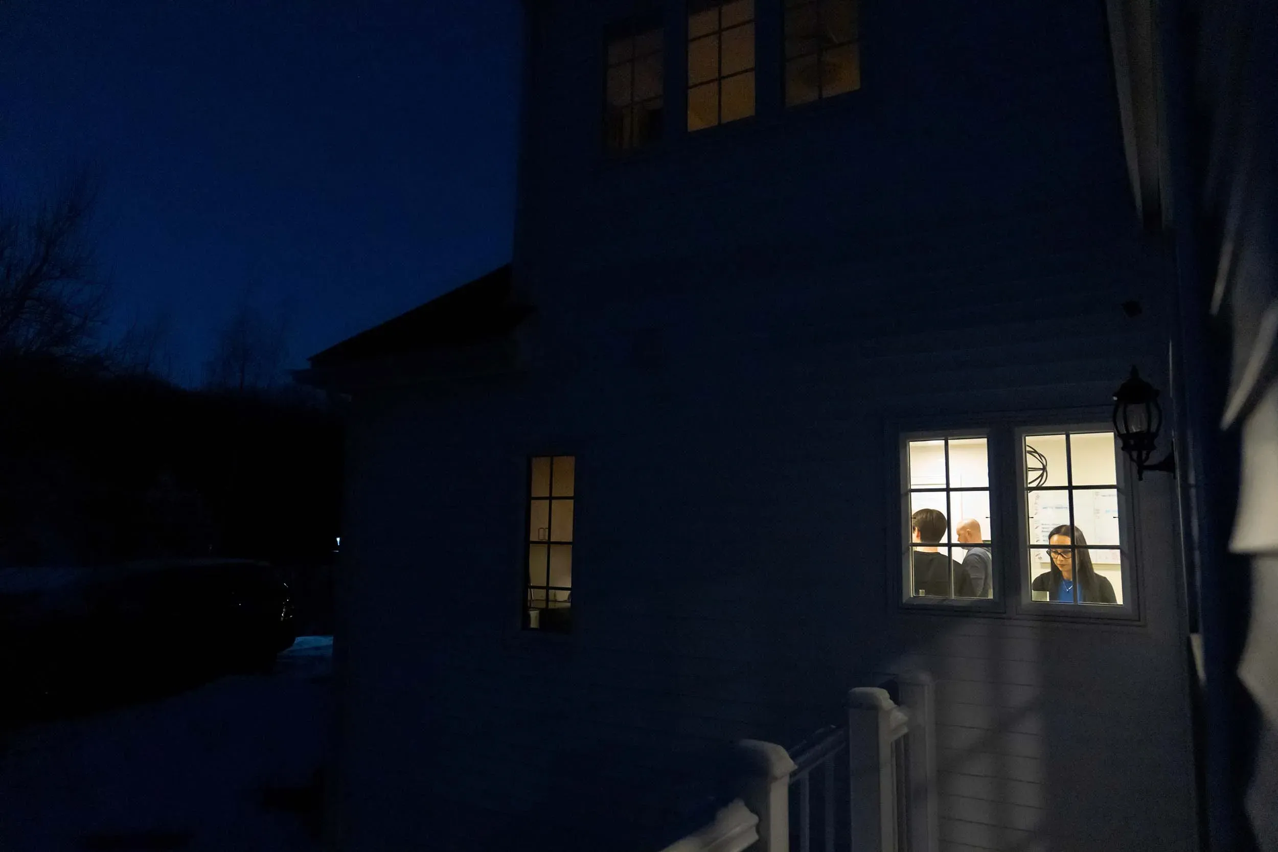 مجموعة من الأشخاص يتحدثون داخل غرفة مضاءة، بينما يظهر الظلام الخارجي، مما يعكس شعور العزلة والتحديات التي تواجه مرضى المناعة الذاتية مثل مرض الذئبة.