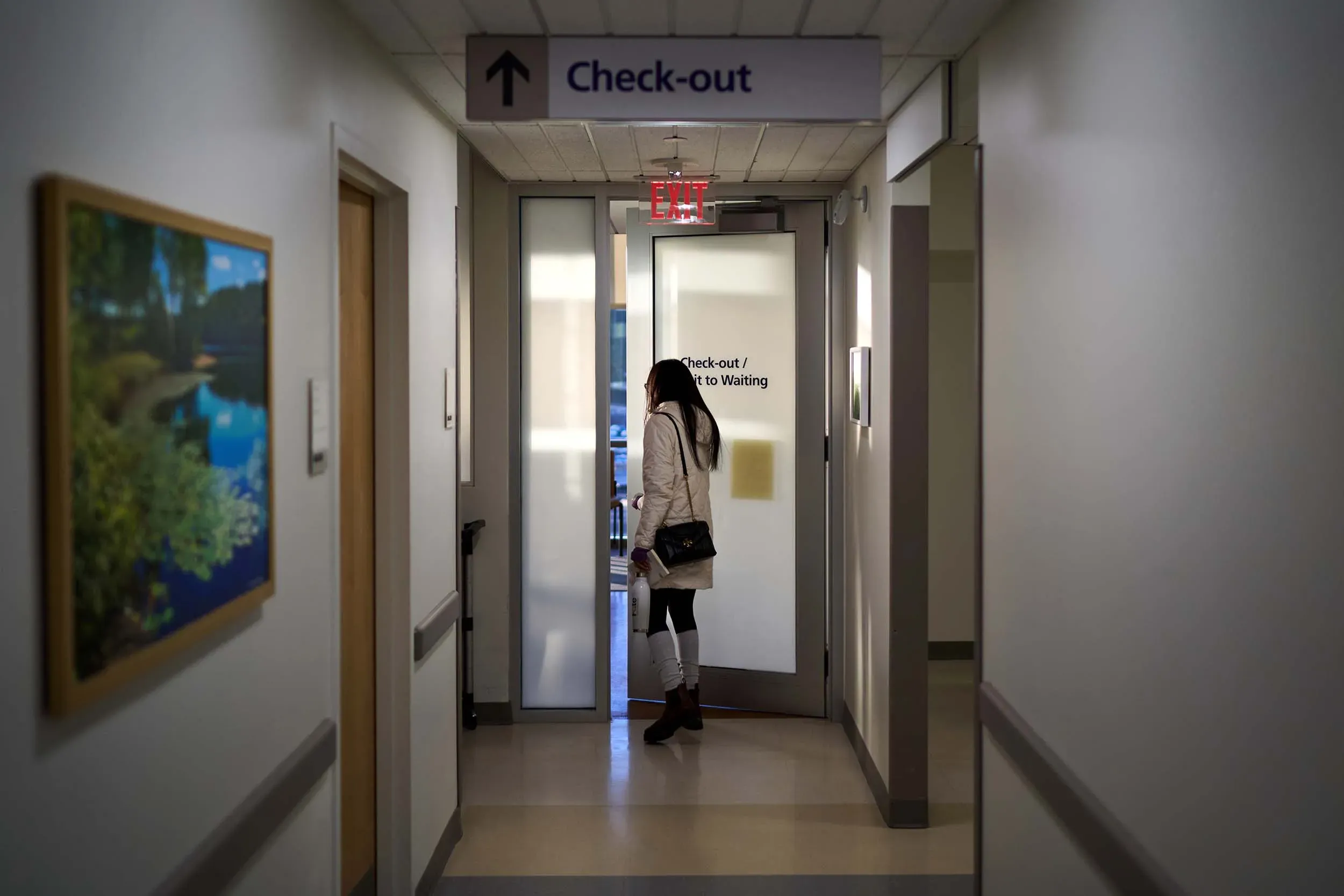 امرأة تقف أمام باب الخروج في مستشفى، تعكس معاناتها في البحث عن تشخيص دقيق لمرض الذئبة، وسط أجواء مهنية.