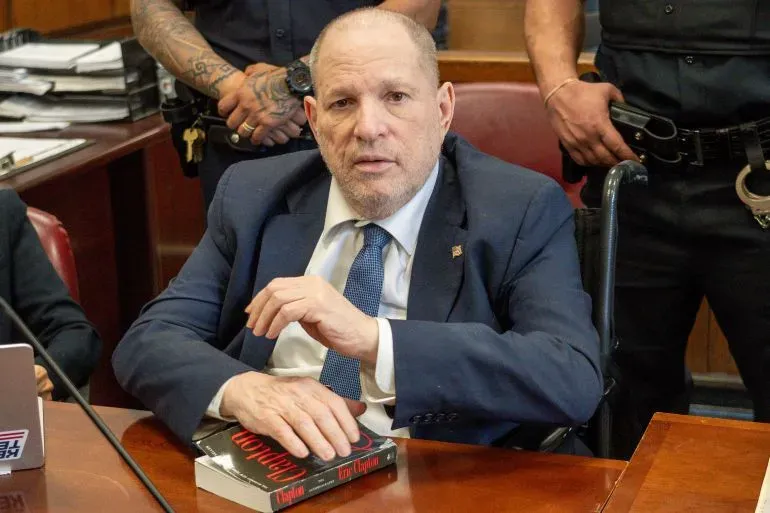 هارفي واينستين، في قاعة المحكمة على كرسي متحرك، مع كتاب في يده، خلال إعادة محاكمته بتهم الاعتداء الجنسي.