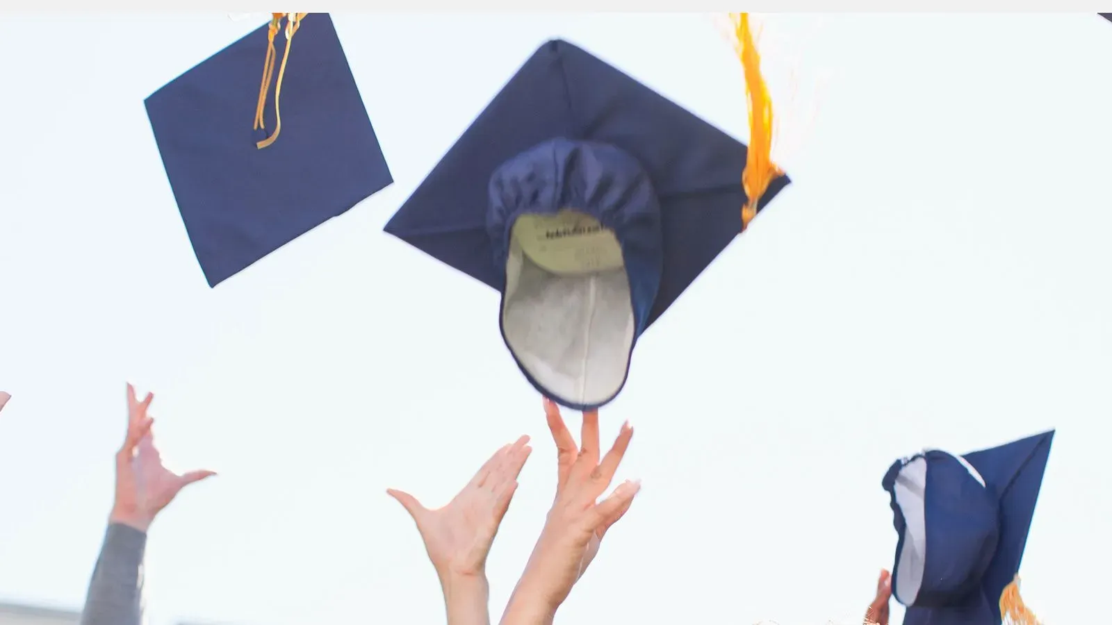 قبعات تخرج تُلقى في الهواء من قبل خريجين، تعبيرًا عن الفرح والاحتفال بالإنجاز الأكاديمي وسط تحديات مستقبلية في قروض الطلاب.