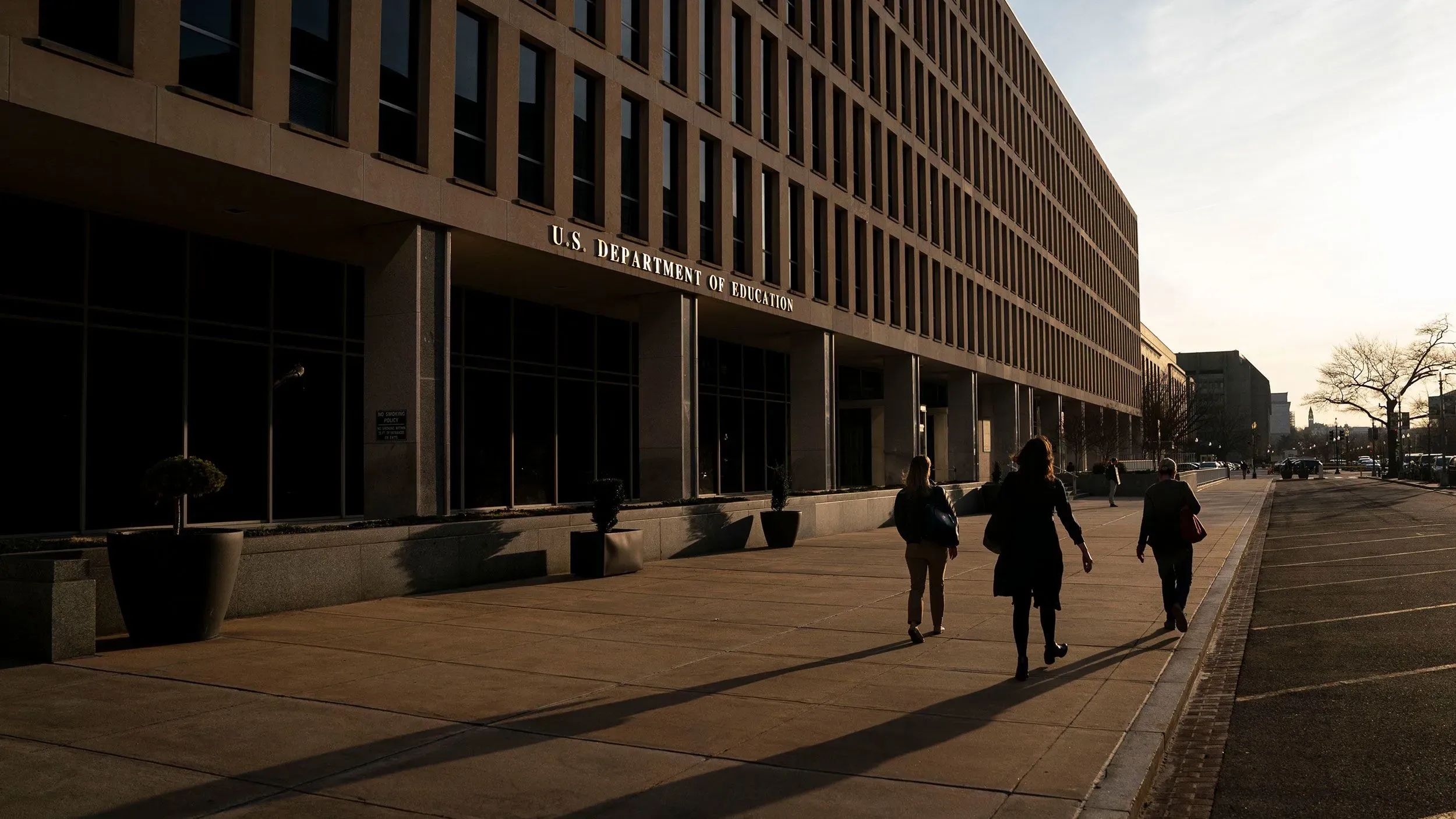 مبنى وزارة التعليم الأمريكية يظهر في الصورة، مع أشخاص يمشون على الرصيف في وقت الغروب، مما يعكس القلق بشأن مستقبل التعليم لذوي الاحتياجات الخاصة.