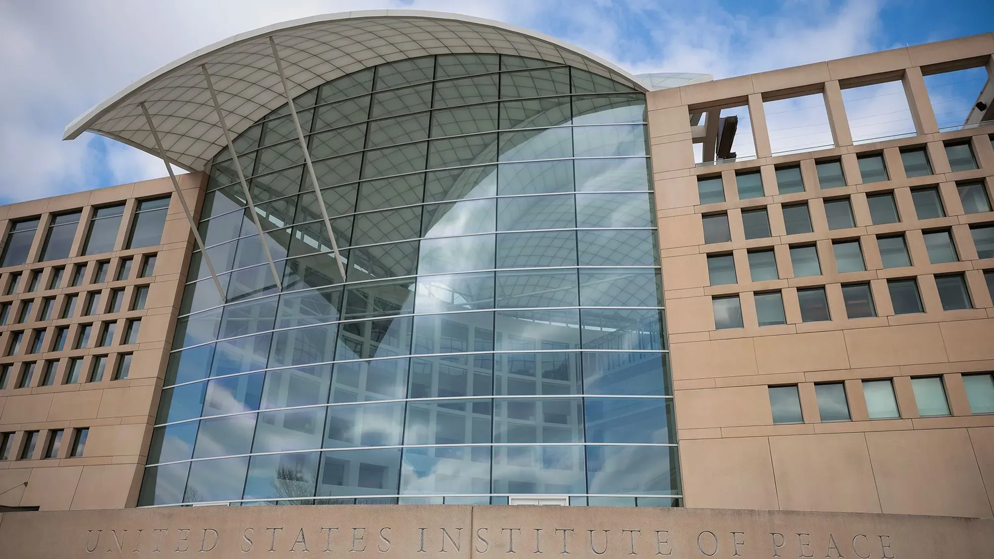 واجهة معهد السلام الأمريكي، تظهر تصميمه المعماري الحديث مع زجاج كبير وسقف مقوس، في سياق تصعيد الأحداث القانونية والإدارية.
