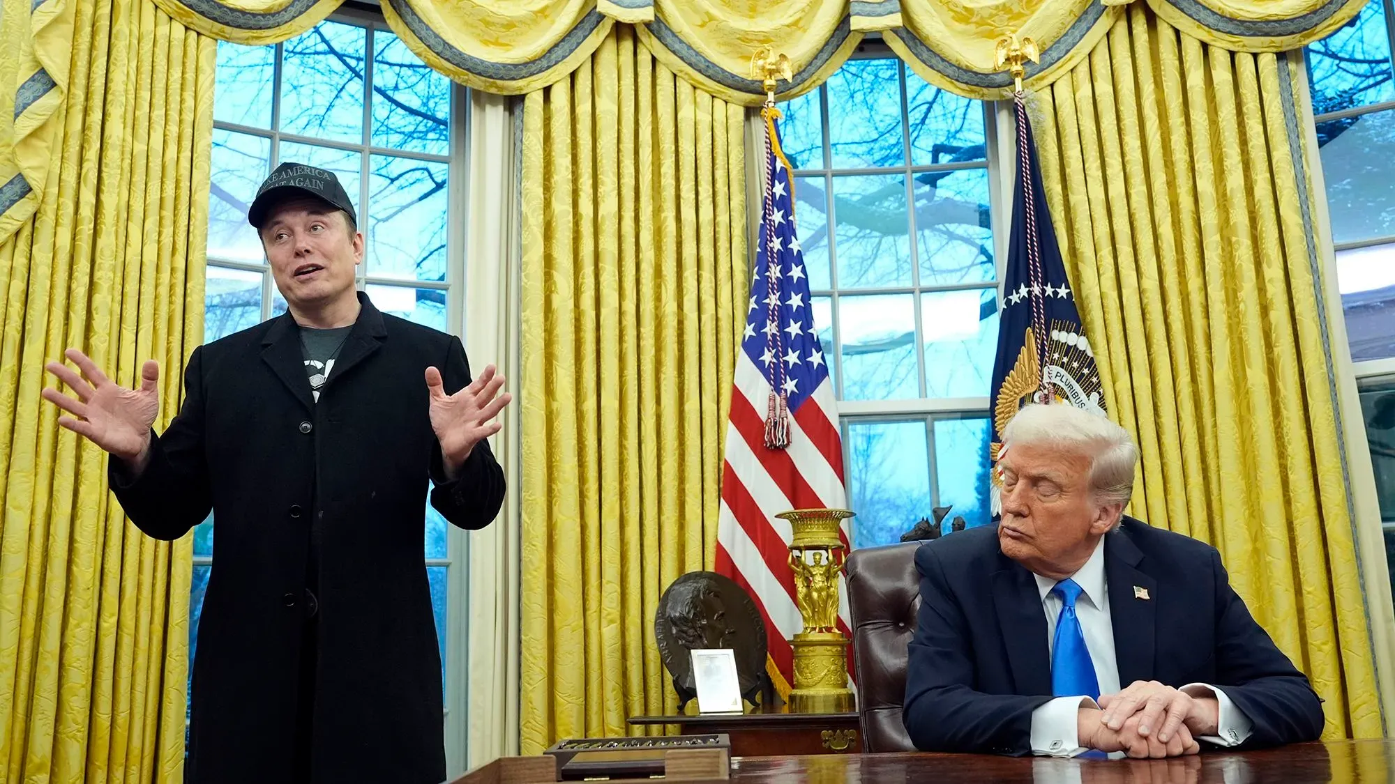 إيلون ماسك يتحدث أثناء اجتماع في المكتب البيضاوي مع دونالد ترامب، وسط أجواء رسمية وزخارف ذهبية.