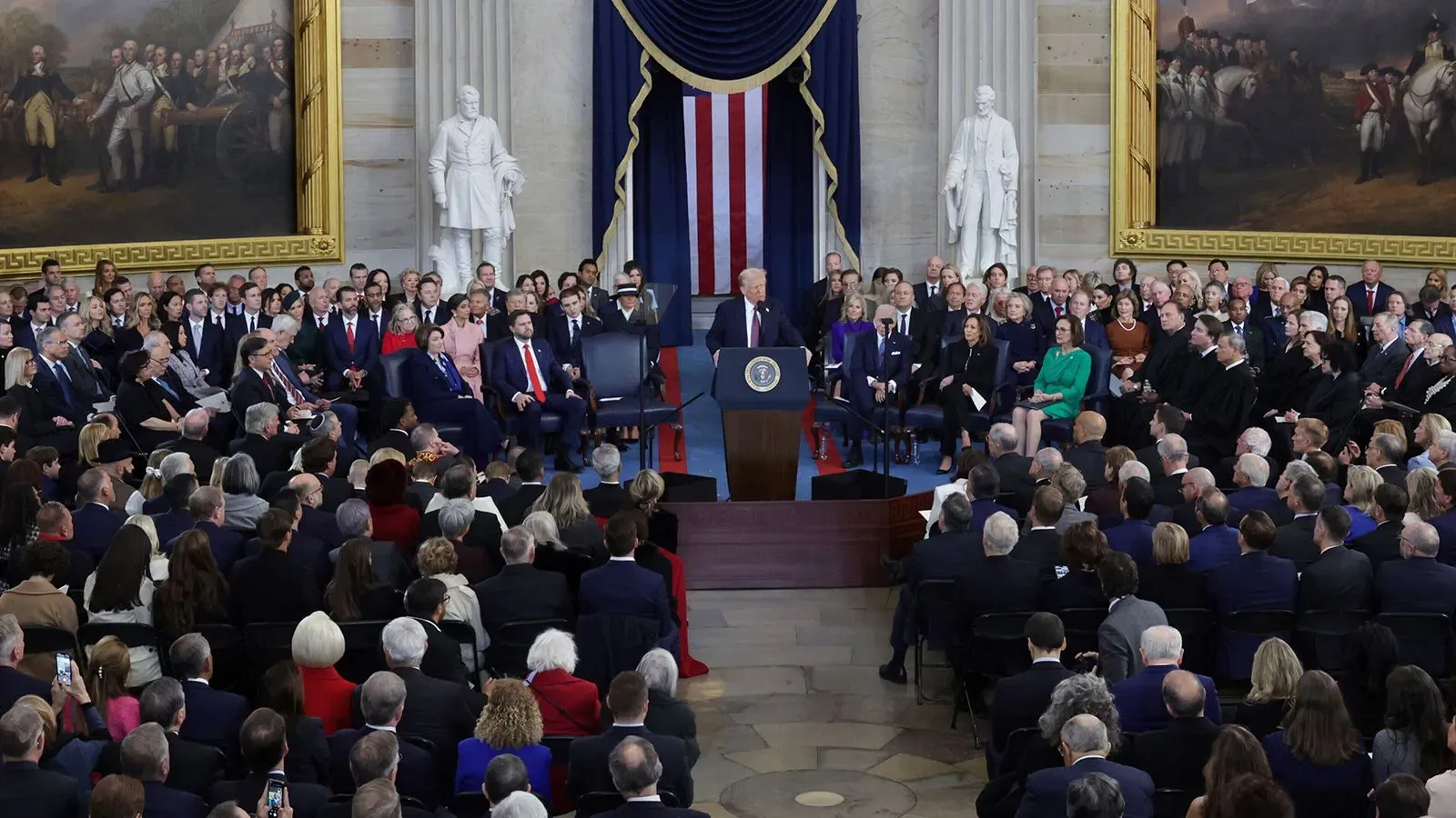 احتفال تنصيب الرئيس دونالد ترامب في مبنى الكابيتول، حيث يتحدث أمام جمهور كبير، مع وجود شخصيات بارزة في الخلفية.