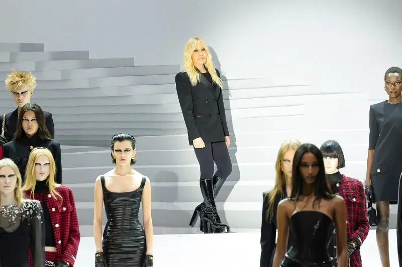 دوناتيلا فيرساتشي تقف بفخر خلف عارضات الأزياء خلال عرض أزياء فيرساتشي في ميلانو، مع لمسة من الأناقة والتميز.