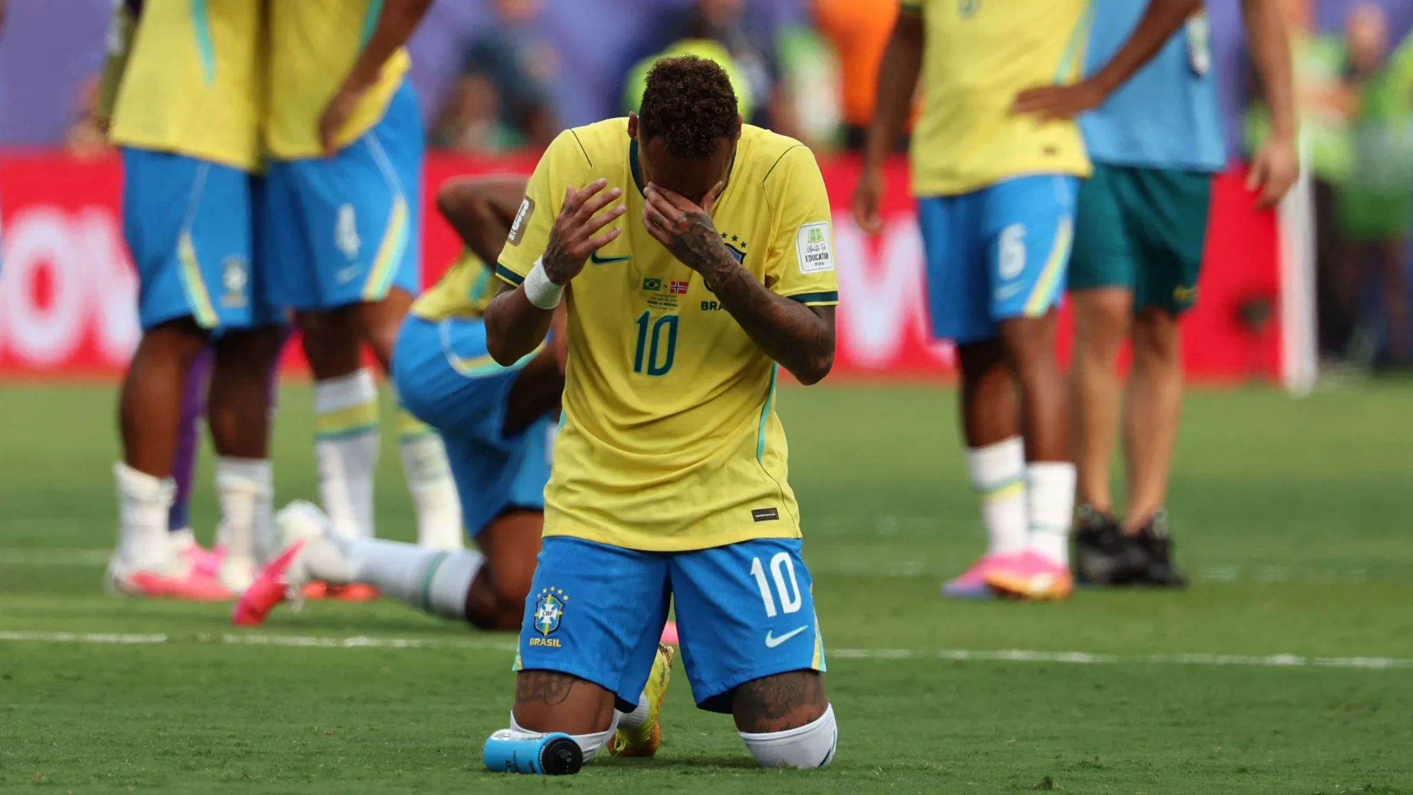 نيمار جالس على ركبتيه بحزن بعد خروج البرازيل من كأس العالم، مع لاعبين آخرين في الخلفية، يعكس ألم الخسارة والإصابات.