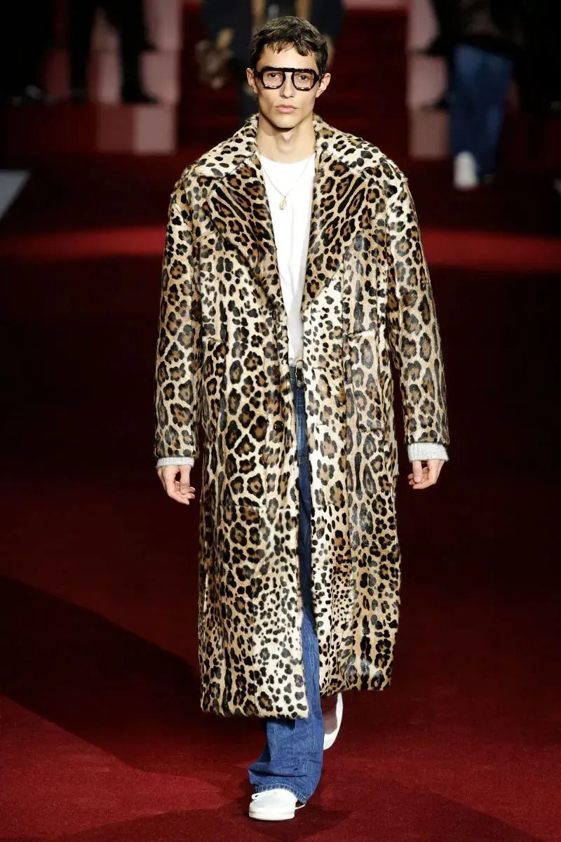 عارض أزياء يرتدي معطفًا مزخرفًا بنقشة النمر مع طقم جينز وأحذية رياضية، يطل على منصة عرض أزياء ميلانو لصيف 2025.